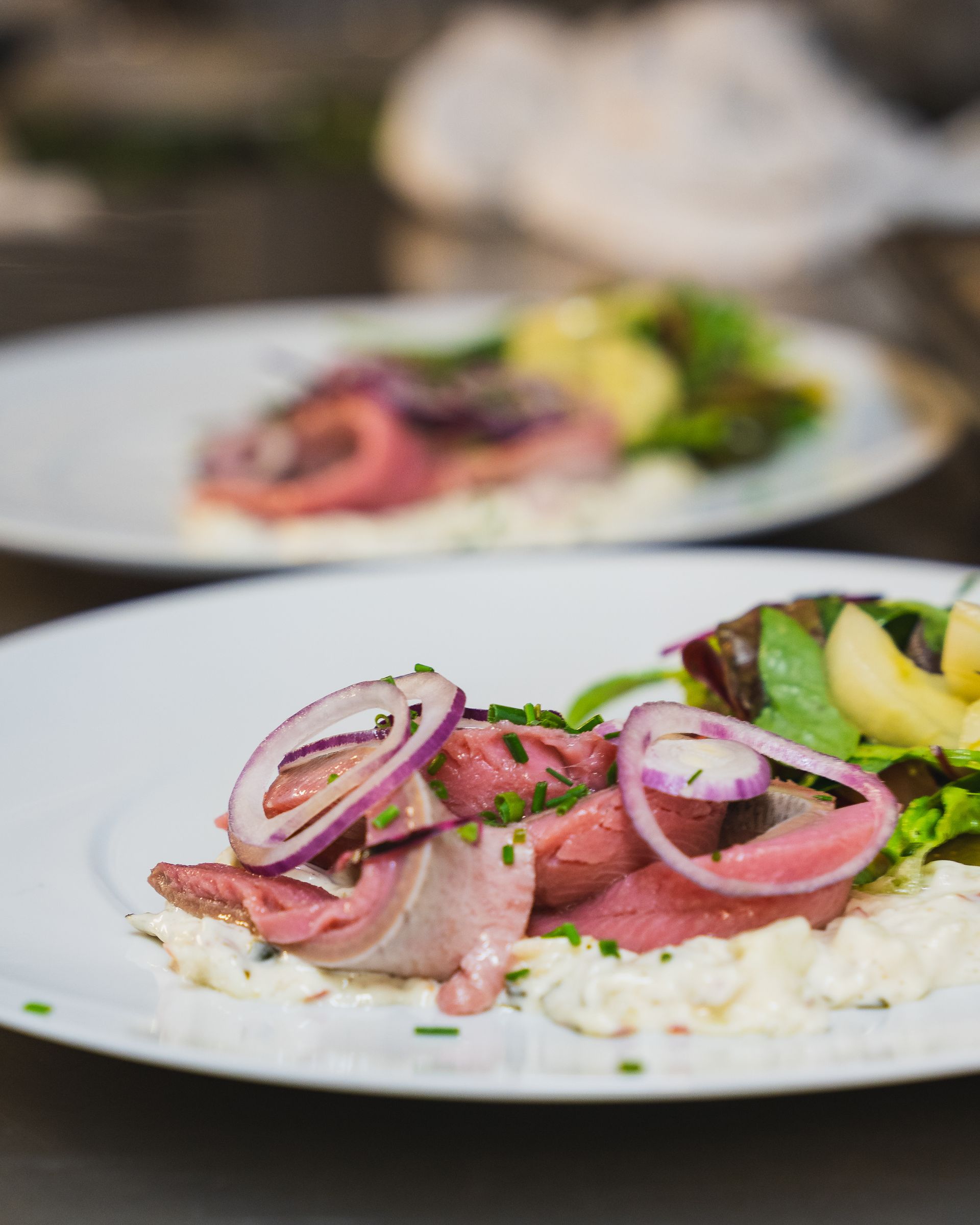 Zwei Teller mit Essen: dünn geschnittenes Fleisch mit roten Zwiebeln, Sahne, Salat und Kartoffeln.