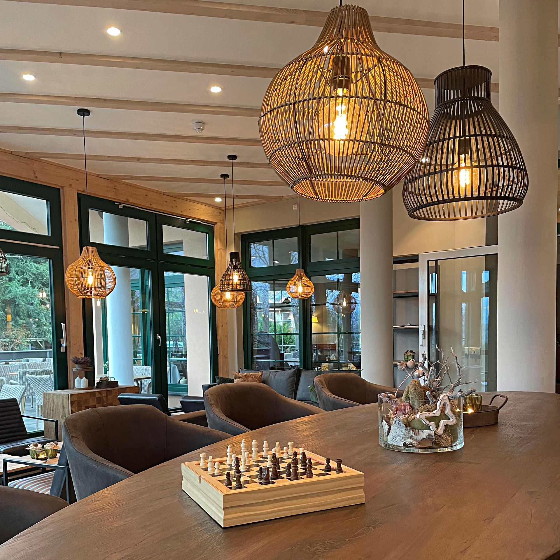 Innenbereich mit Bar, Schachspiel, hängenden Korblampen und Fenstern mit Blick ins Grüne.