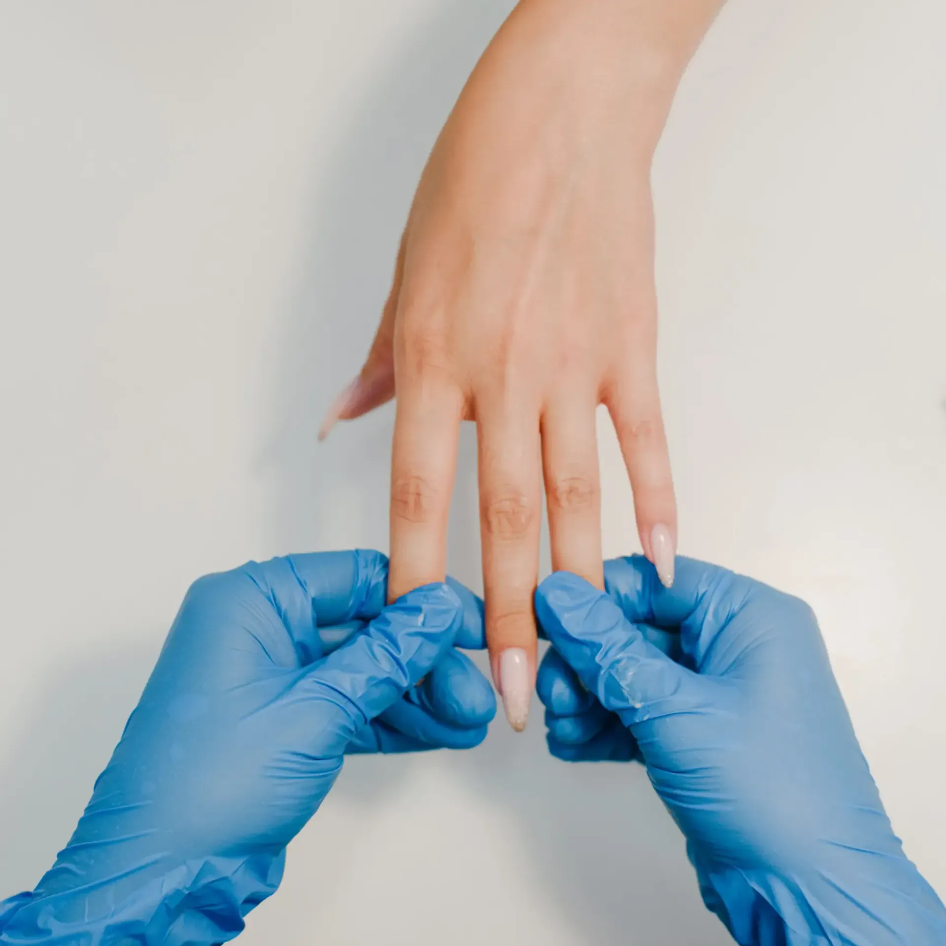 Manos con uñas largas, una de ellas sostenida por manos enguantadas.