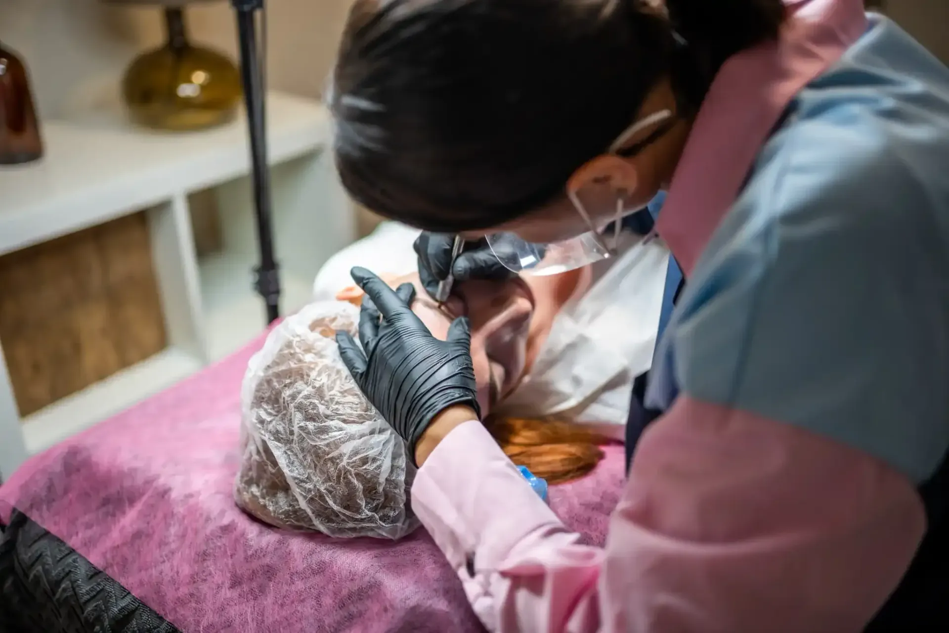 Persona que se somete a un procedimiento cosmético de cejas. El técnico, con guantes y lupa.
