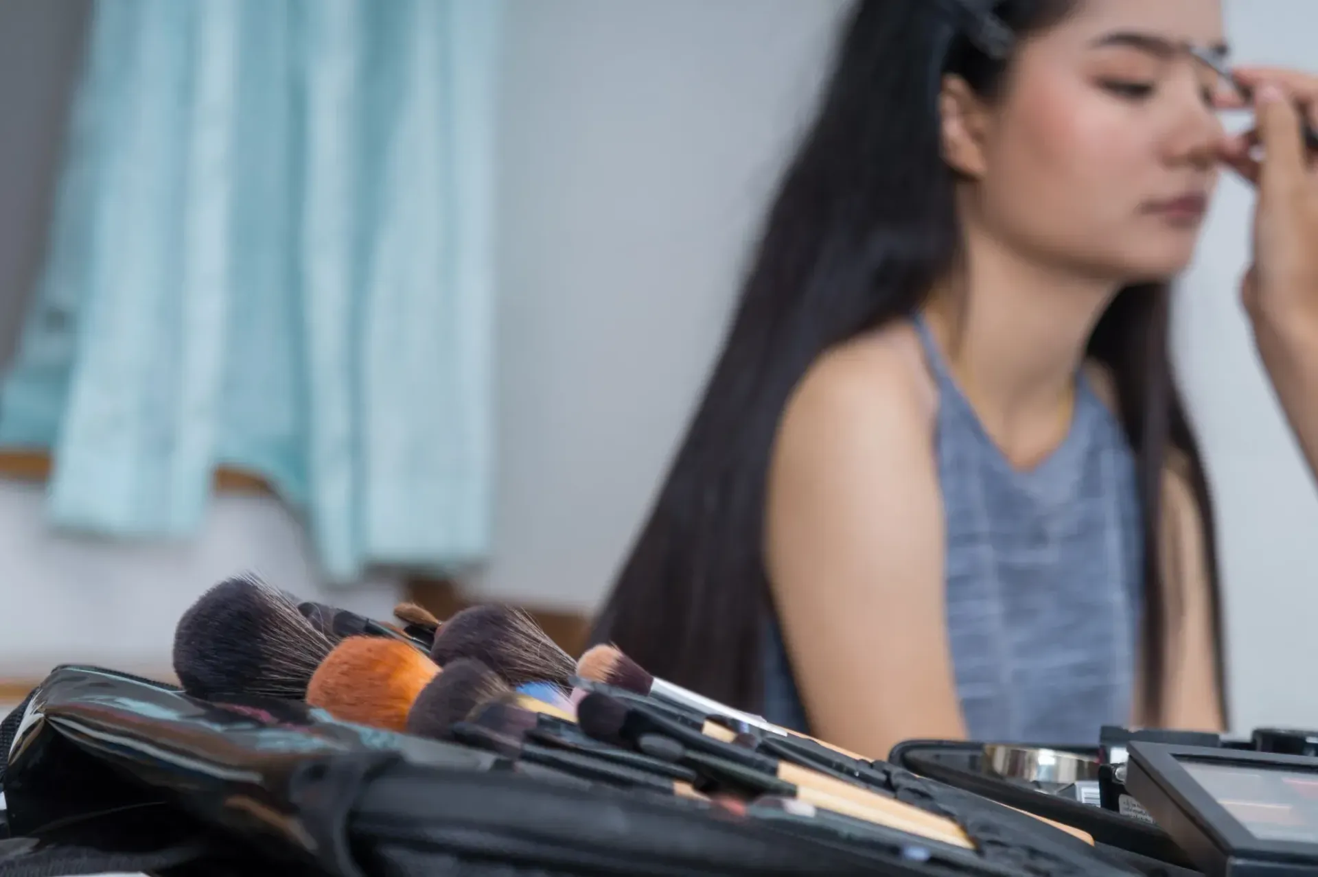 Maquilladora aplicando maquillaje a una persona, con pinceles en primer plano.