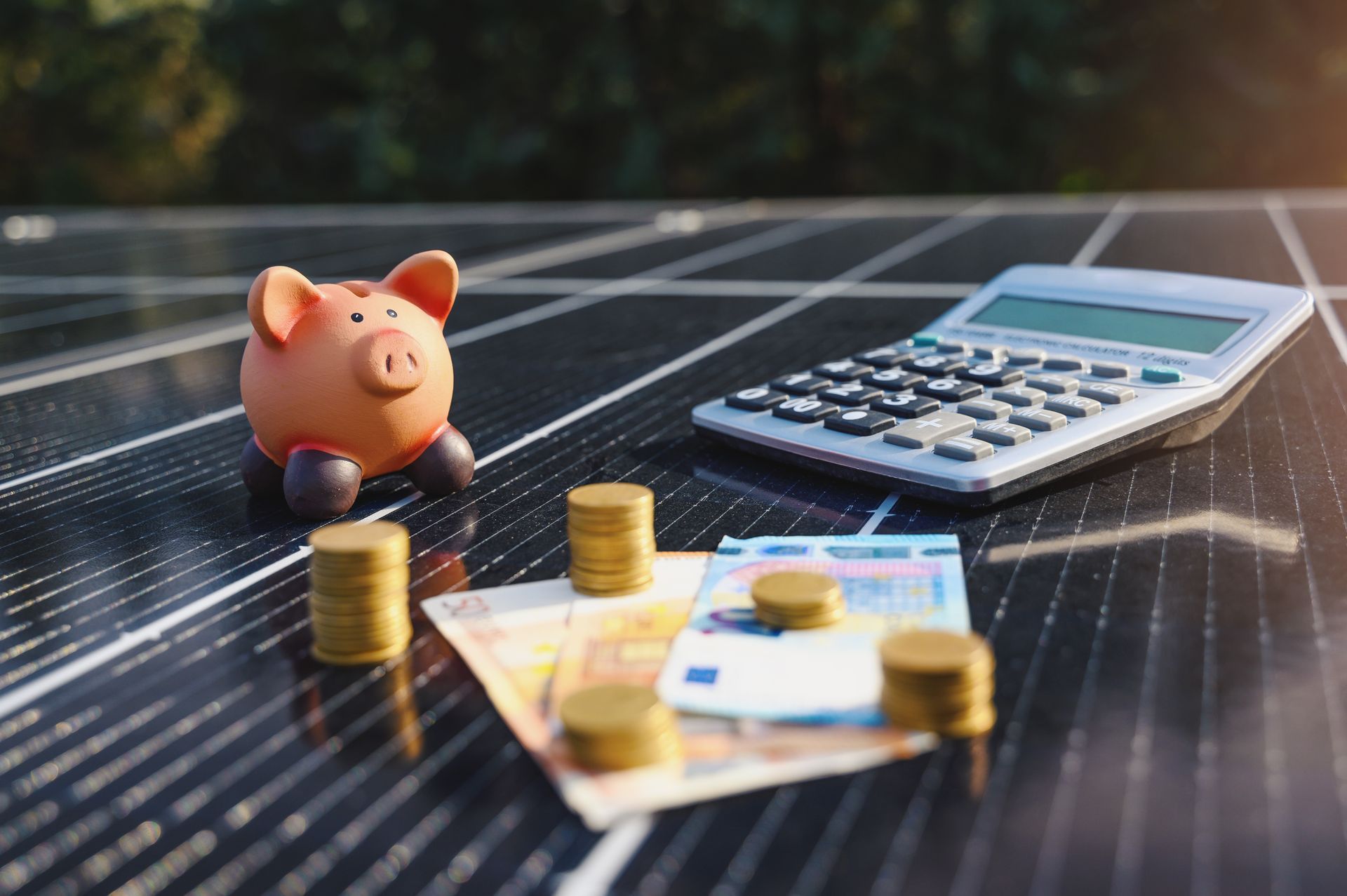 Pièces, billets, calculatrice et tirelire posés sur un panneau solaire.