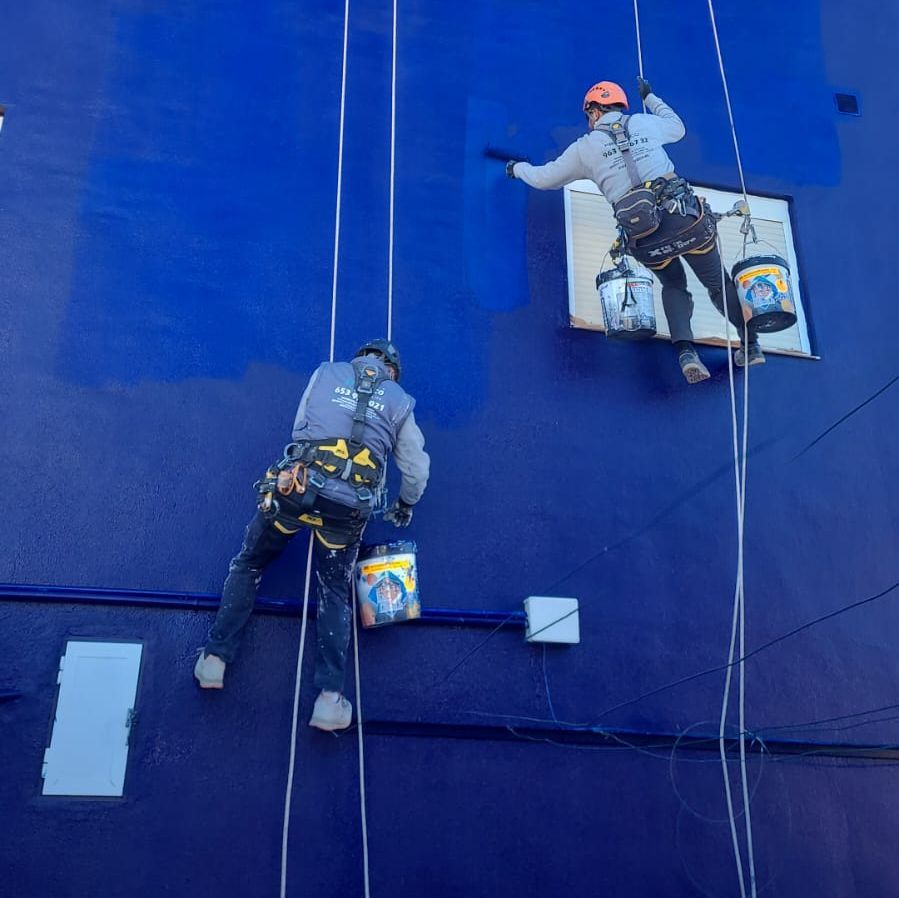 Dos hombres están pintando un edificio azul con baldes de pintura.