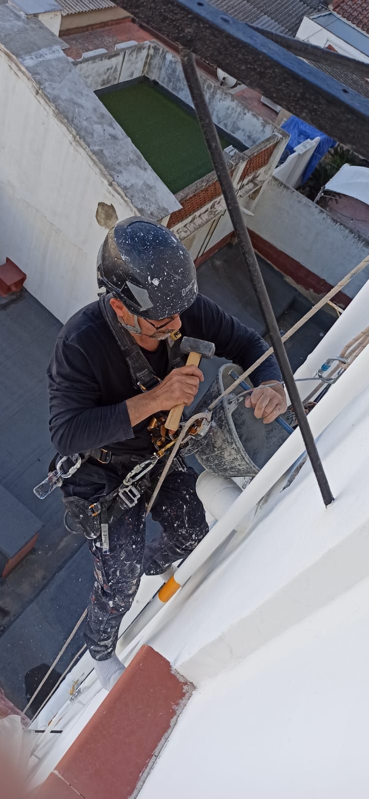 Un hombre está pintando una pared desde el costado de un edificio.