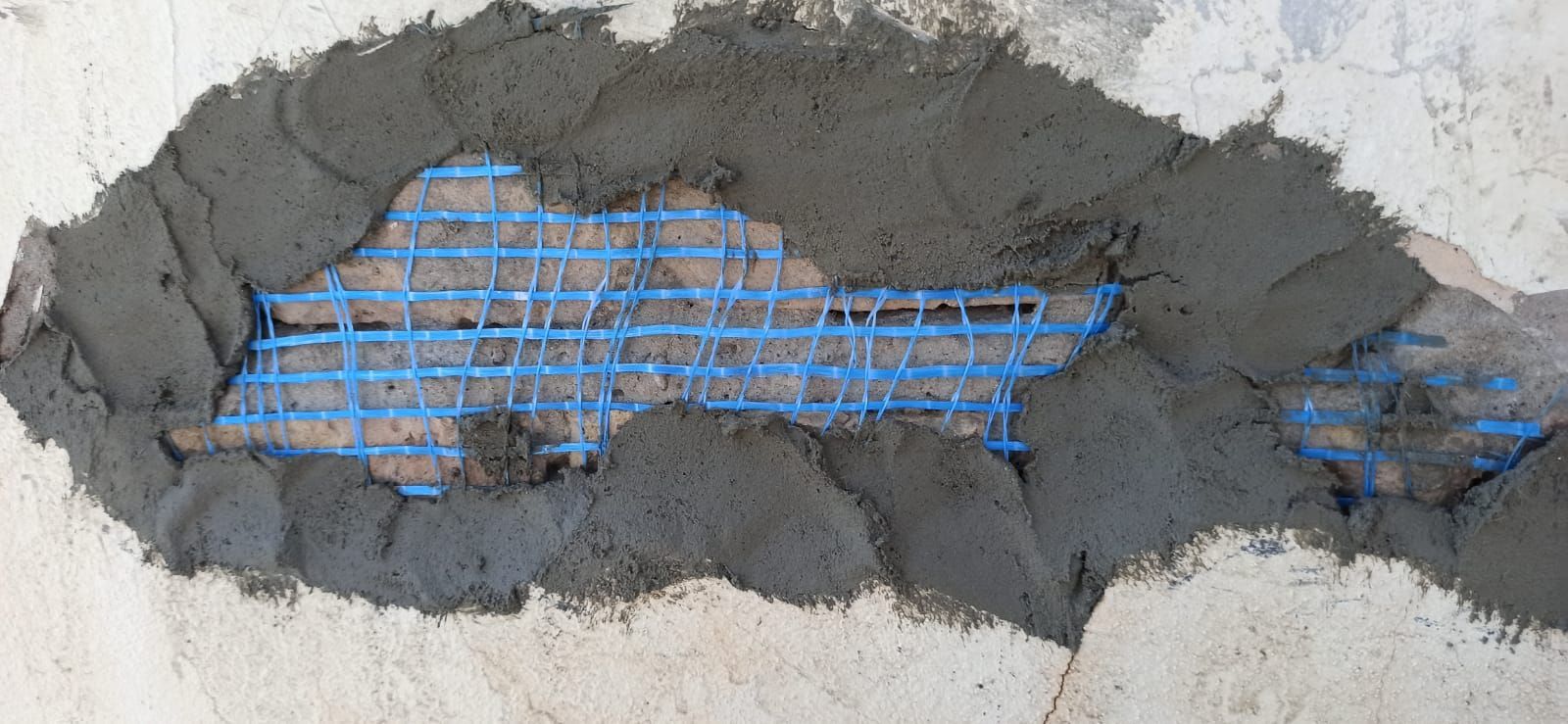 Un agujero en una pared de hormigón con una malla azul cubriéndolo.