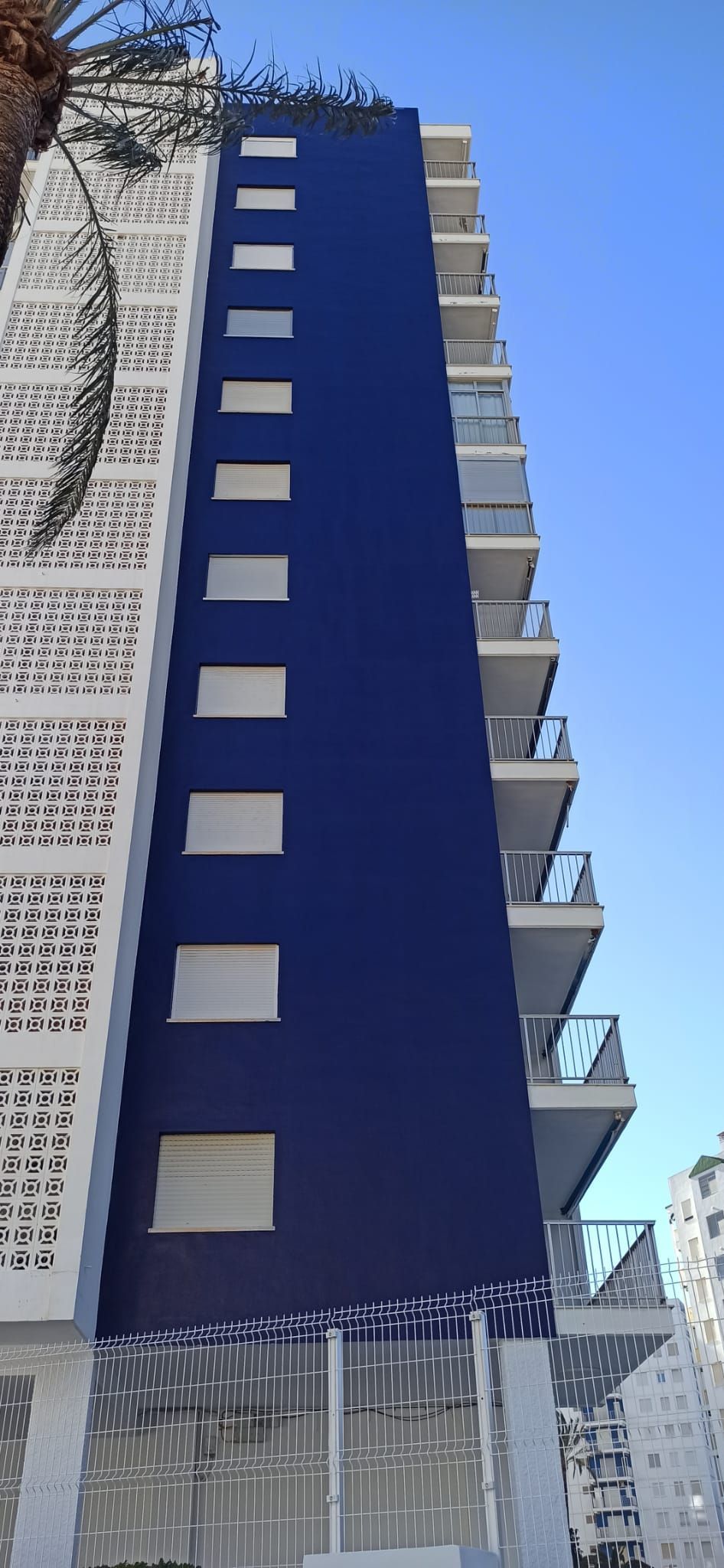 Un edificio azul y blanco con balcones contra un cielo azul.