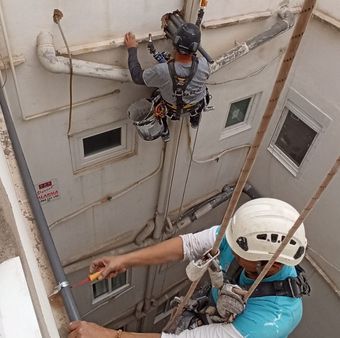 Un hombre que lleva un casco está trabajando en una tubería en el costado de un edificio.