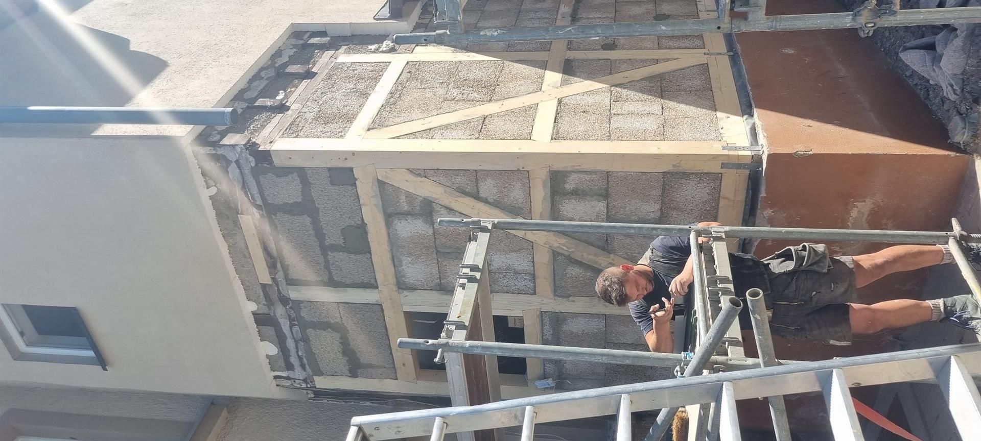 Ein Mann steht auf einer Leiter vor einem im Bau befindlichen Gebäude.