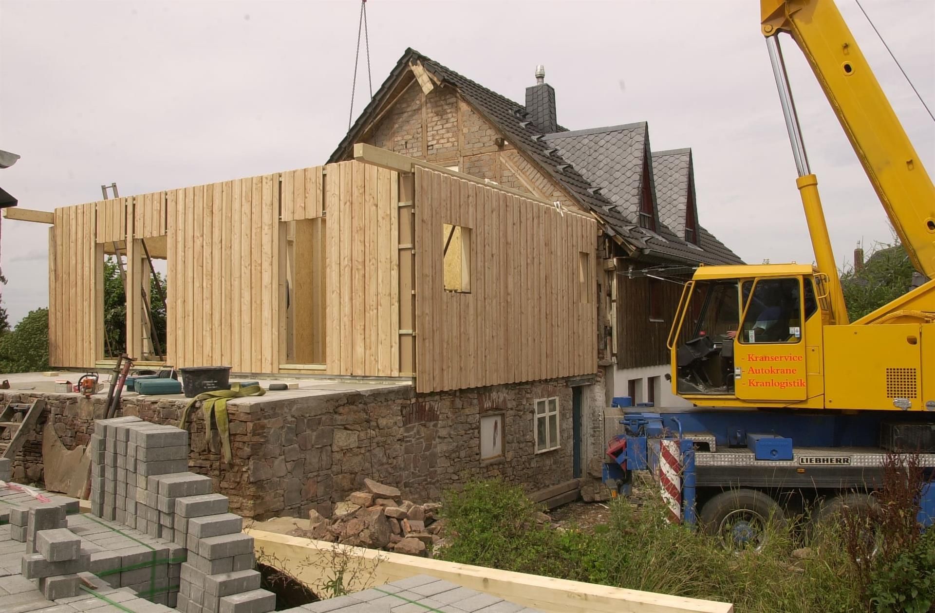 Ein gelb-blauer Kran steht vor einem im Bau befindlichen Haus