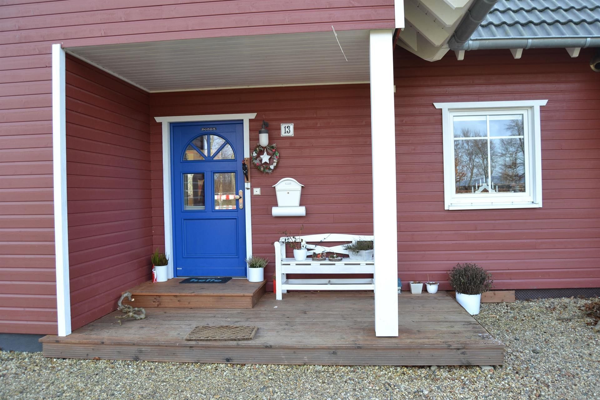 Ein rotes Haus mit einer blauen Tür und einer weißen Bank