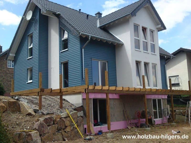 Ein blau-weißes Haus mit der Website www.holzbau-hilgers.de unten