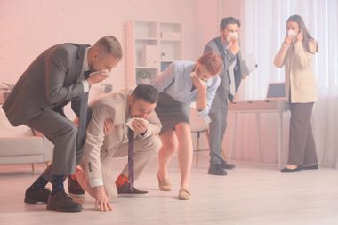 Plusieurs adultes sont accroupis et penchés en avant avec un mouchoir sur leur nez dans un bureau enfumé.