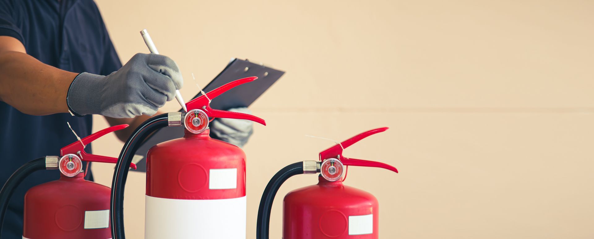 Un technicien inspecte des extincteurs rouges avec des gants dans un environnement intérieur.