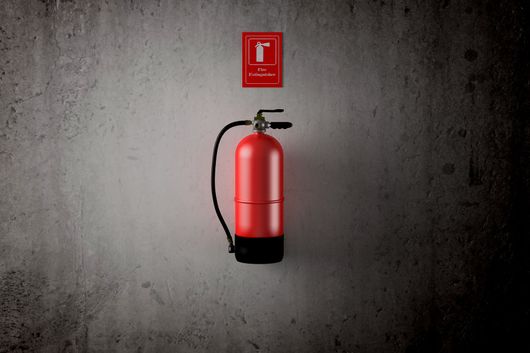 Extincteur rouge fixé sur un mur gris avec un panneau de sécurité incendie au-dessus.