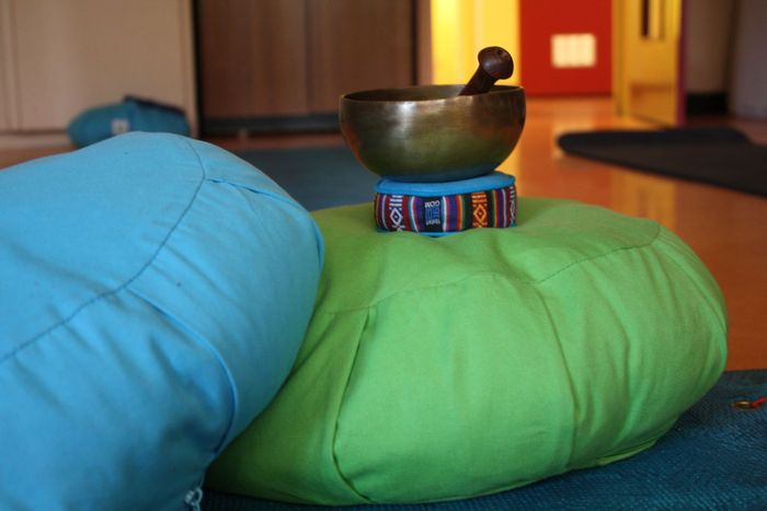 Des coussins bleus et verts avec un bol chantant sur un support coloré, dans une pièce chaleureuse