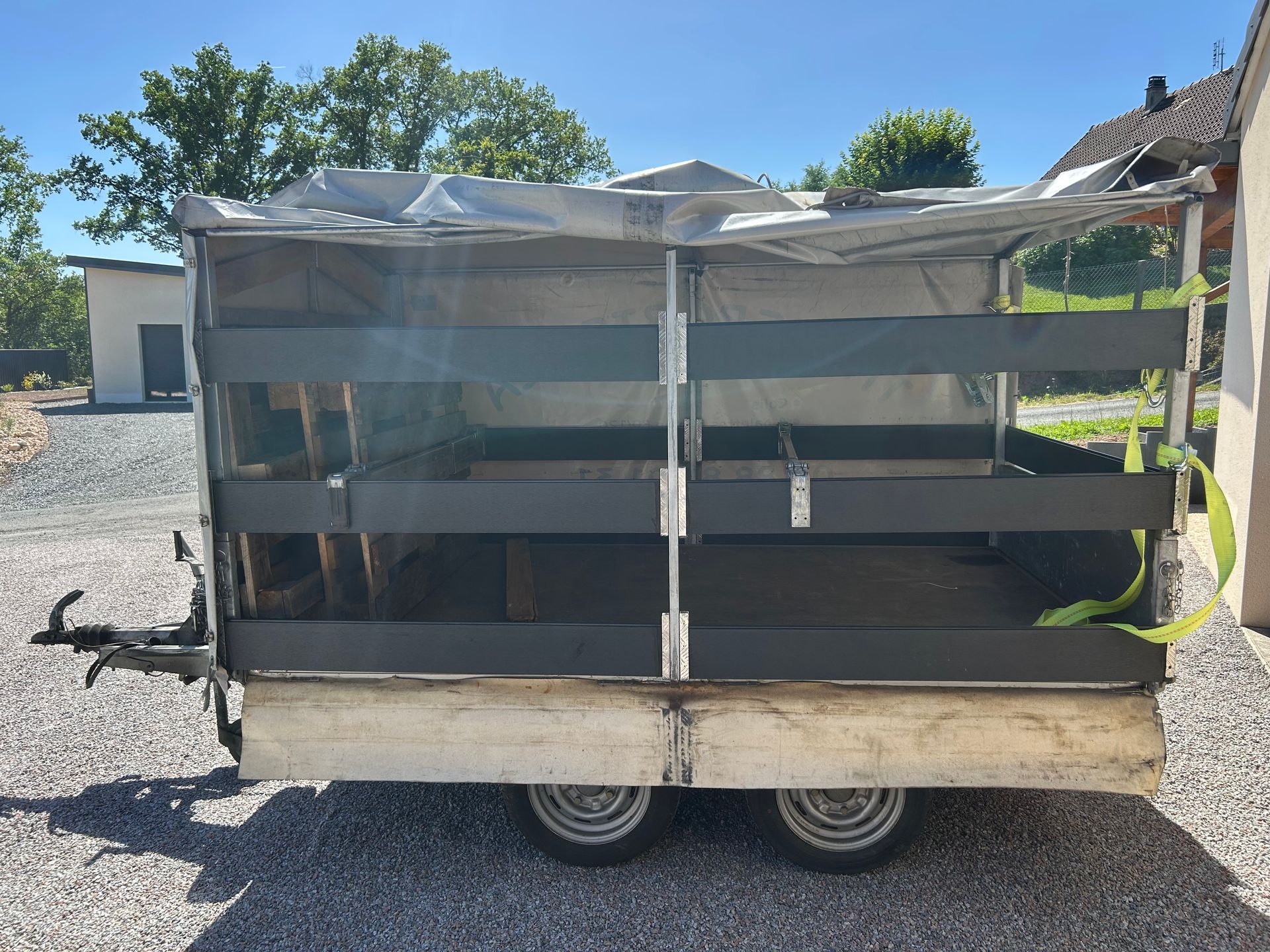 Une camionnette grise tracte une remorque blanche sur un terrain gravillonné.