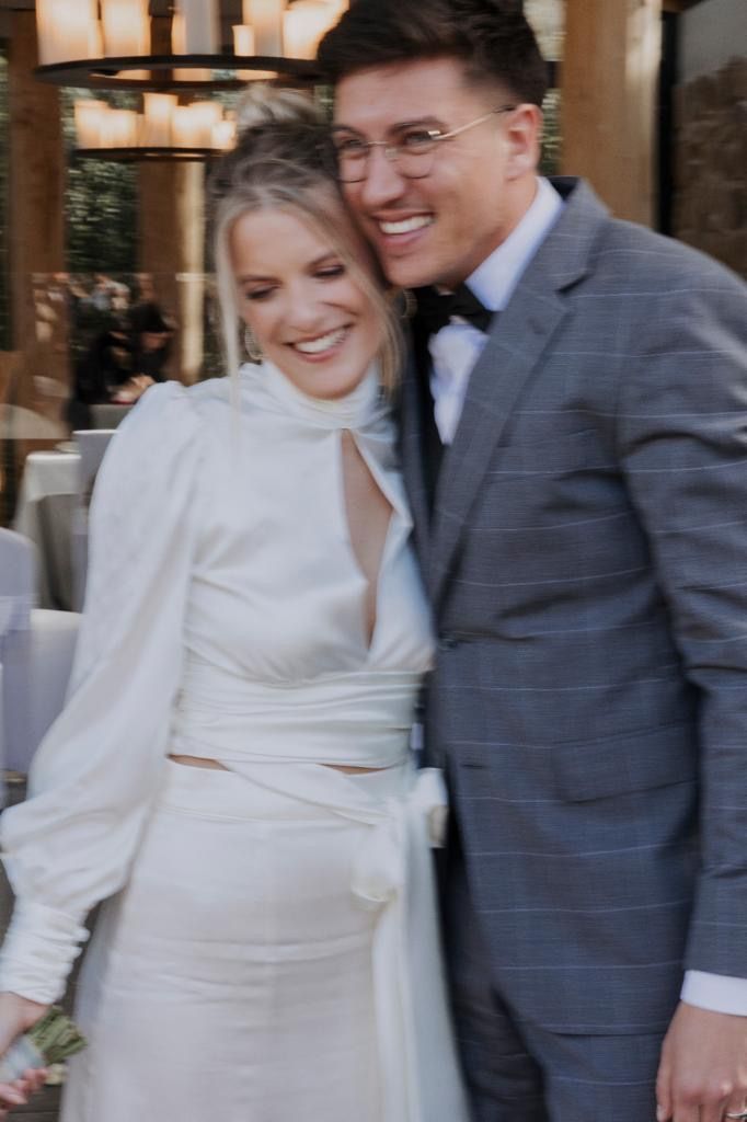 Braut im weißen Kleid und Bräutigam im grauen Anzug umarmen sich und lächeln bei der Hochzeit.