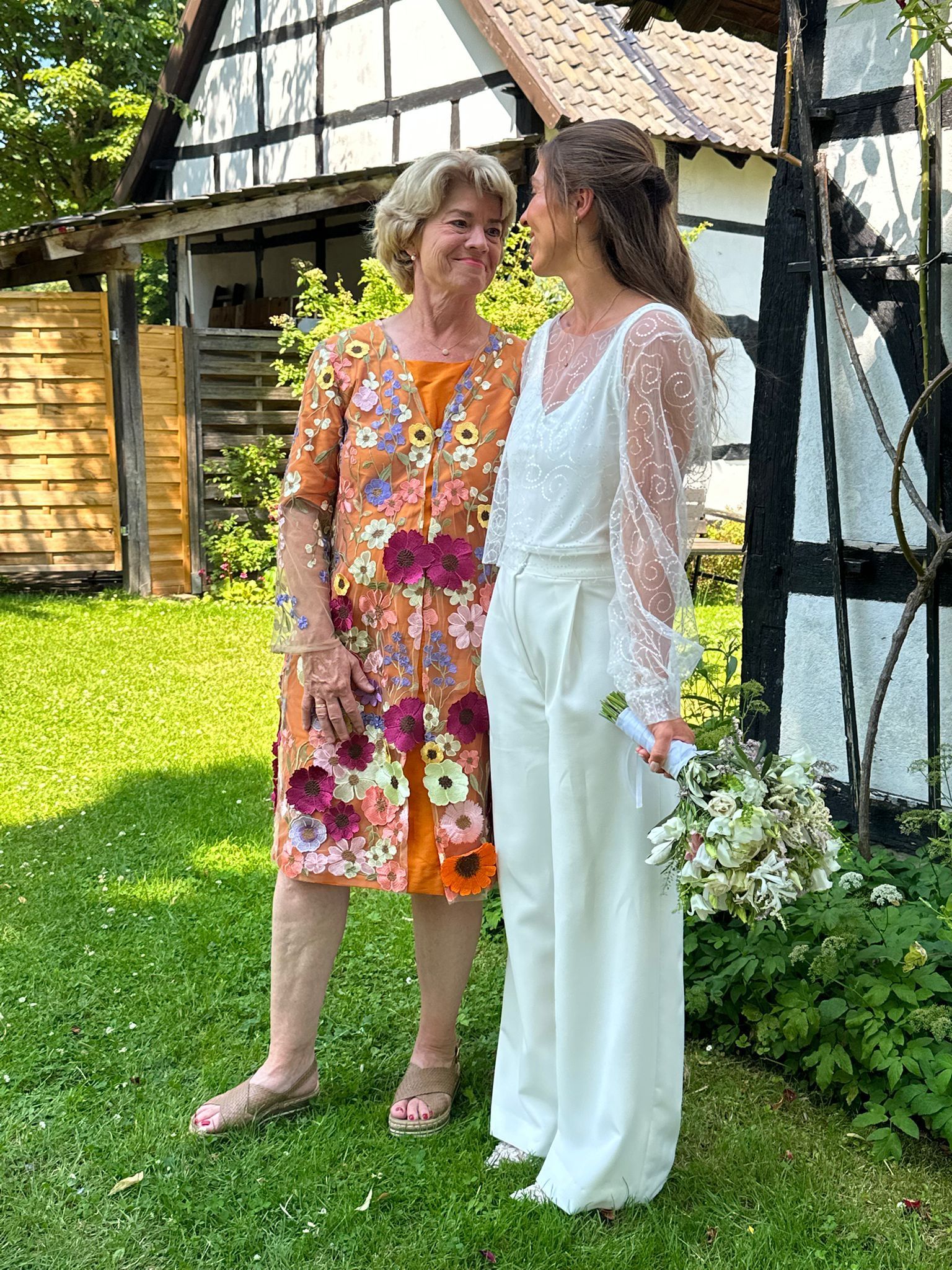 Braut in weißem Zweiteiler mit Mutter in geblütem Kleid