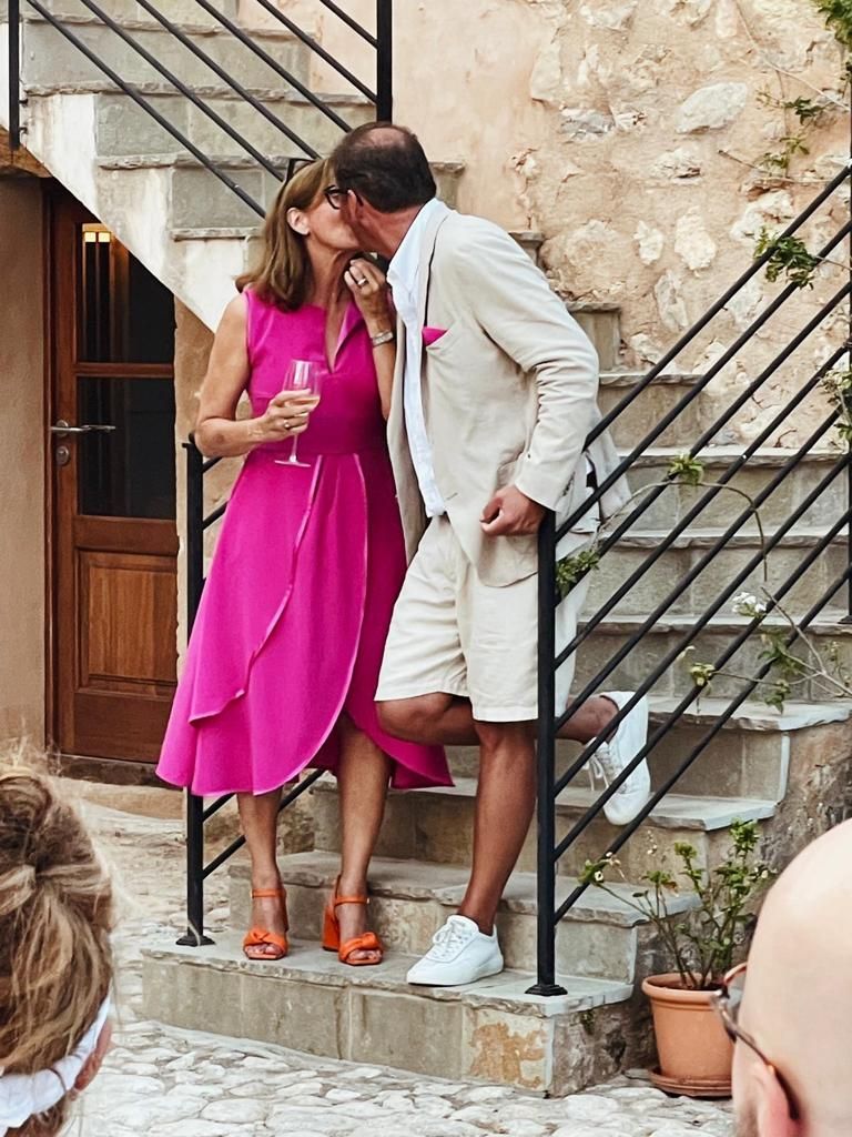 Paar küsst sich auf Steinstufen; Frau im rosa Kleid, Mann im beigen Anzug, im Freien.