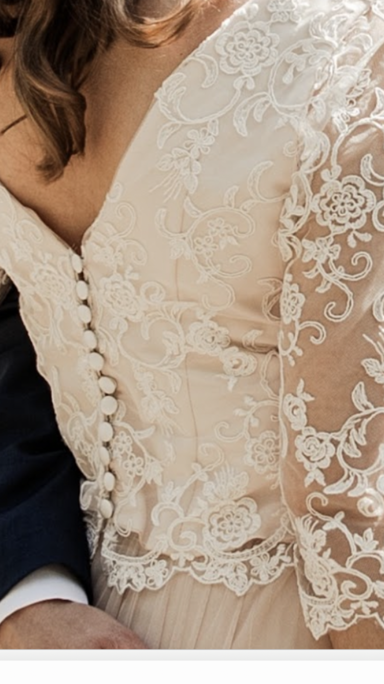 Das Oberteil des cremefarbenen Brautkleides besteht aus Spitze, hat einen Knopfverschluss und lange Ärmel