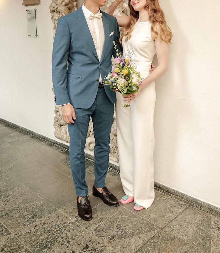 Hochzeitspaar: Braut in weißem Jumpsuit und Bräutigam in taubenblauem Anzug