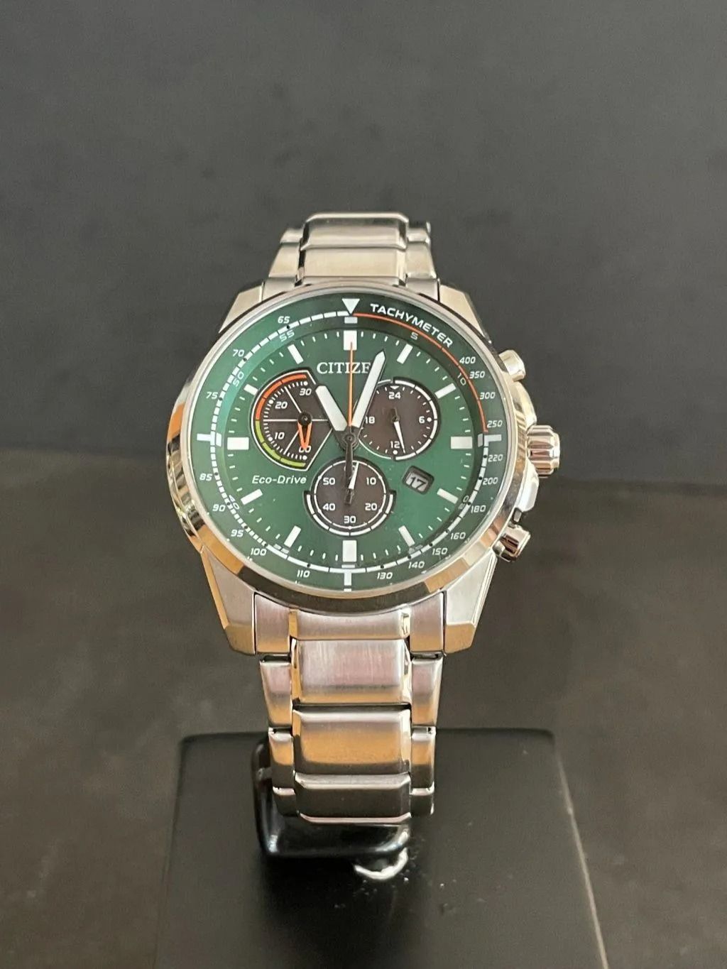 Citizen-Uhr mit grünem Zifferblatt und silbernem Armband, auf einem schwarzen Ständer.