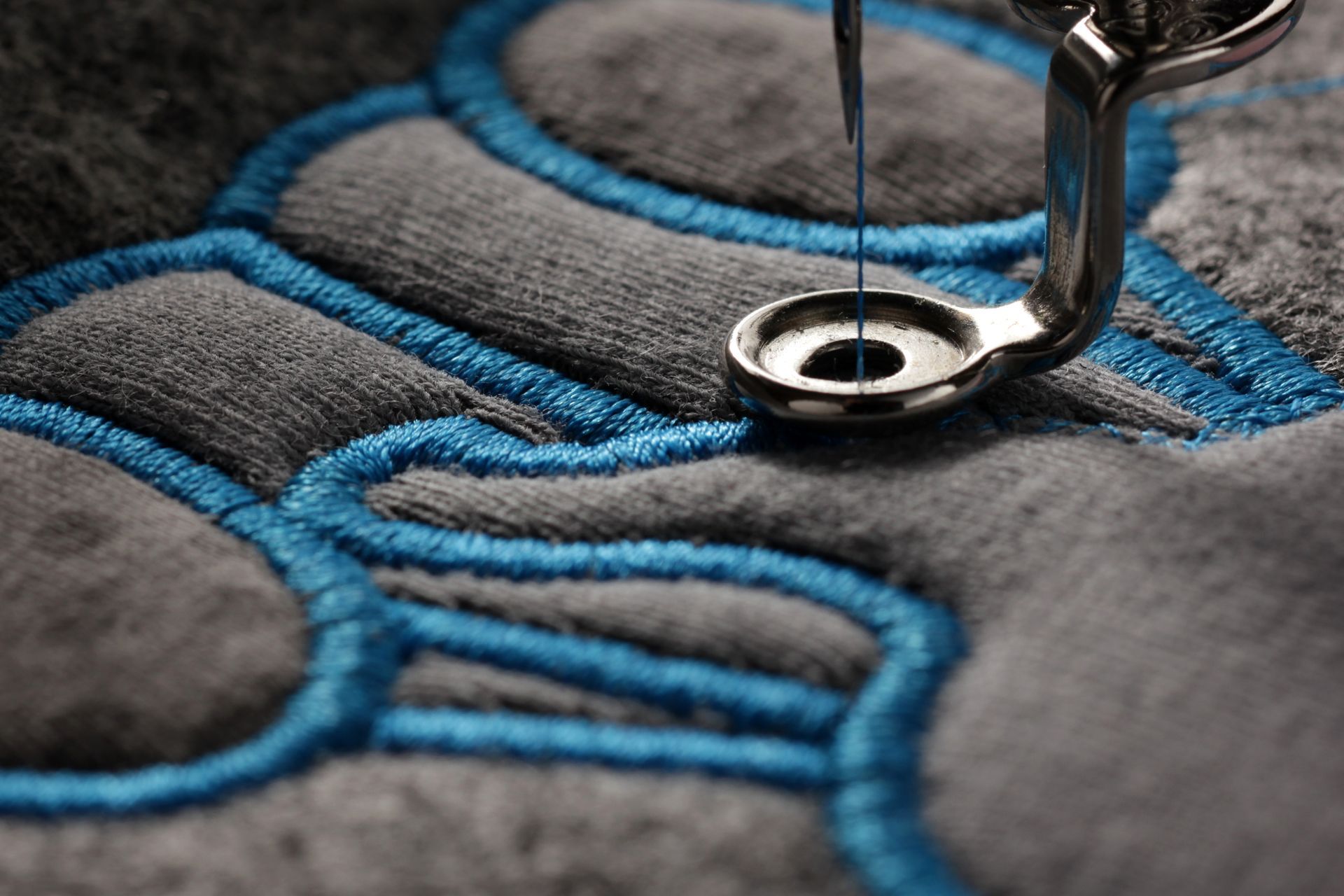 Gros plan d'une aiguille de machine à coudre piquant du fil bleu sur du tissu gris