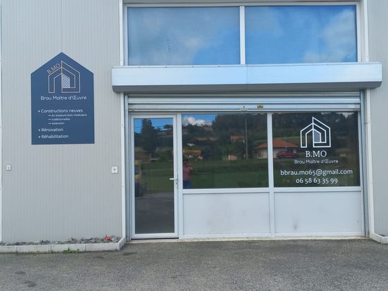 Extérieur d'une façade grise avec porte et fenêtres vitrées, enseigne bleue et entrée pavée.