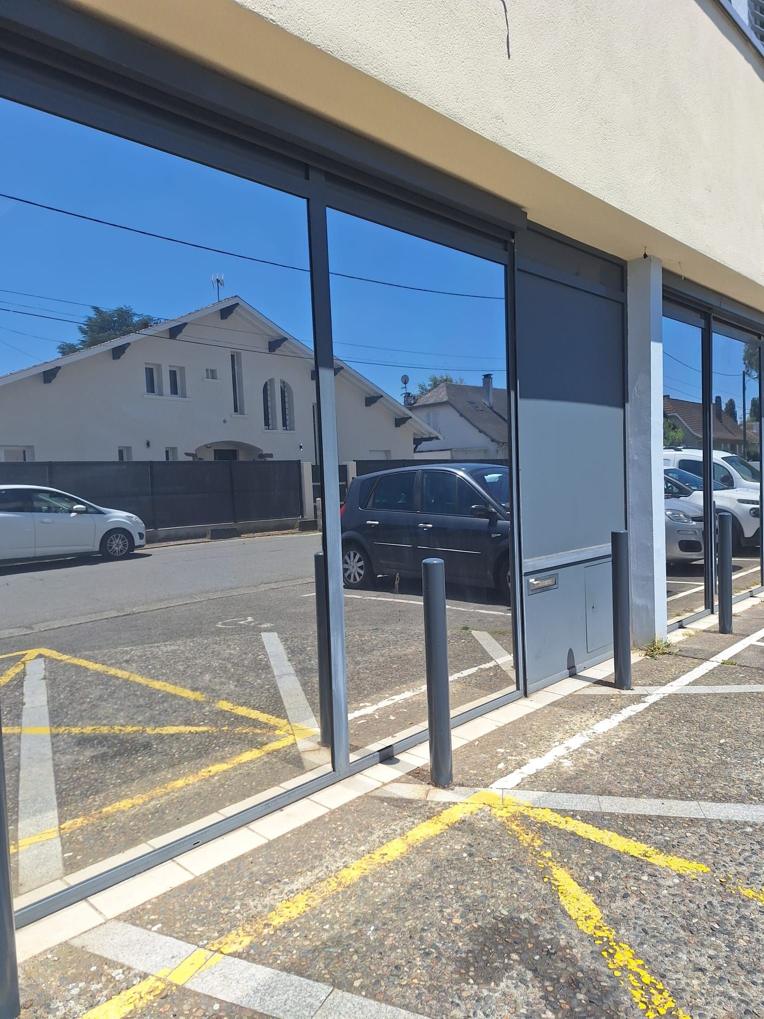 Vitrines reflétant un parking avec des voitures et un ciel bleu, marqué de lignes diagonales jaunes
