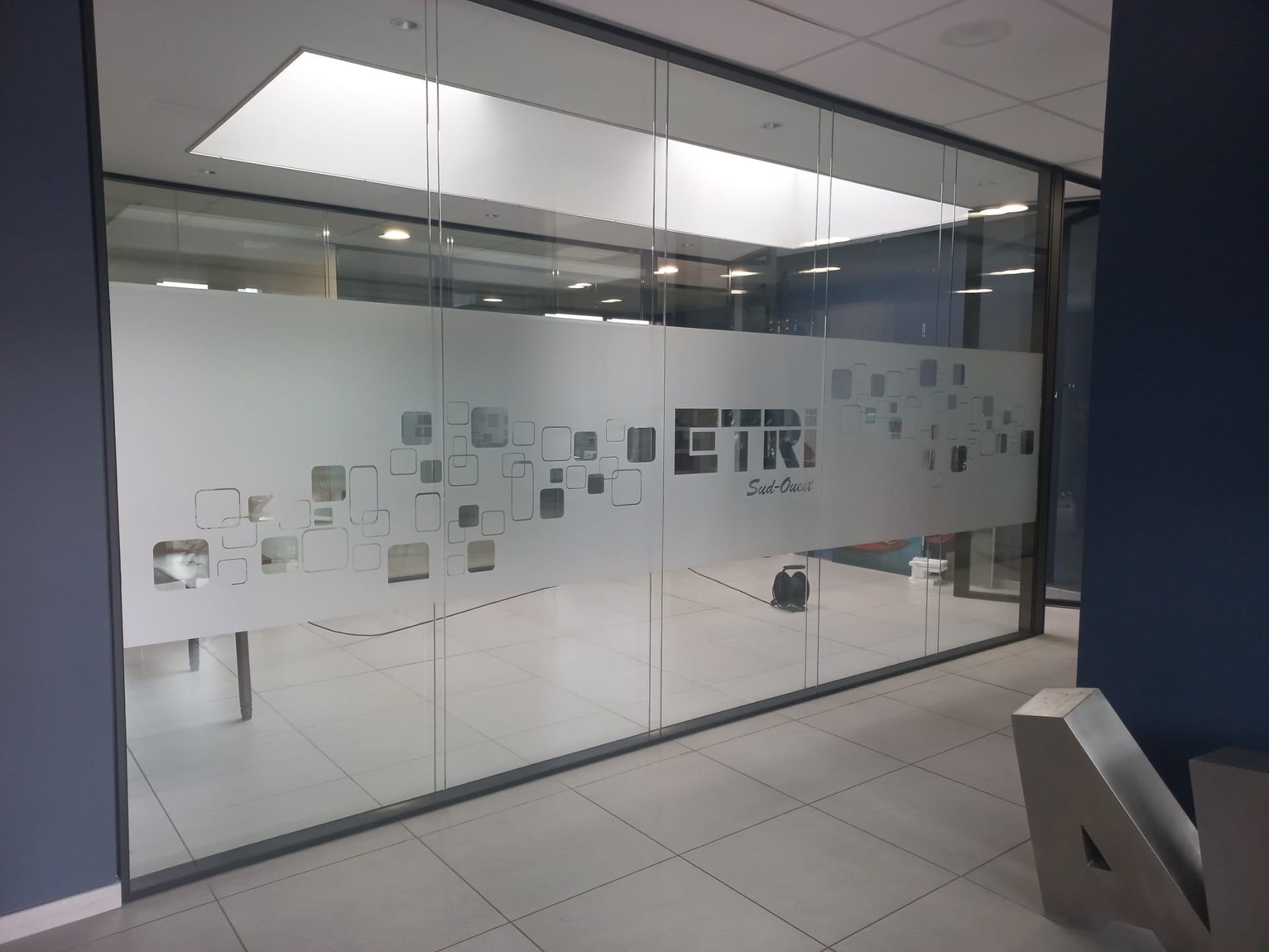 Couloir de bureau aux parois de verre, avec panneaux dépolis et sol carrelé, à l'intérieur d'un bâtiment moderne