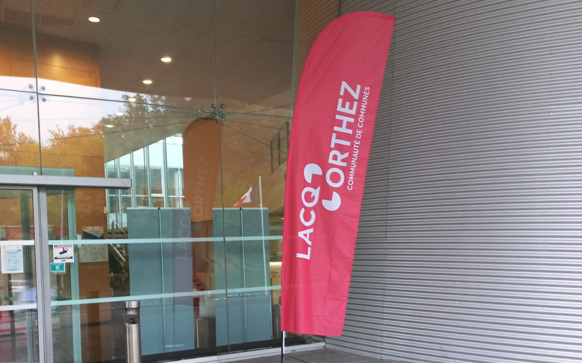 Entrée avec portes vitrées et une banderole rose à côté d'un mur en tôle ondulée grise