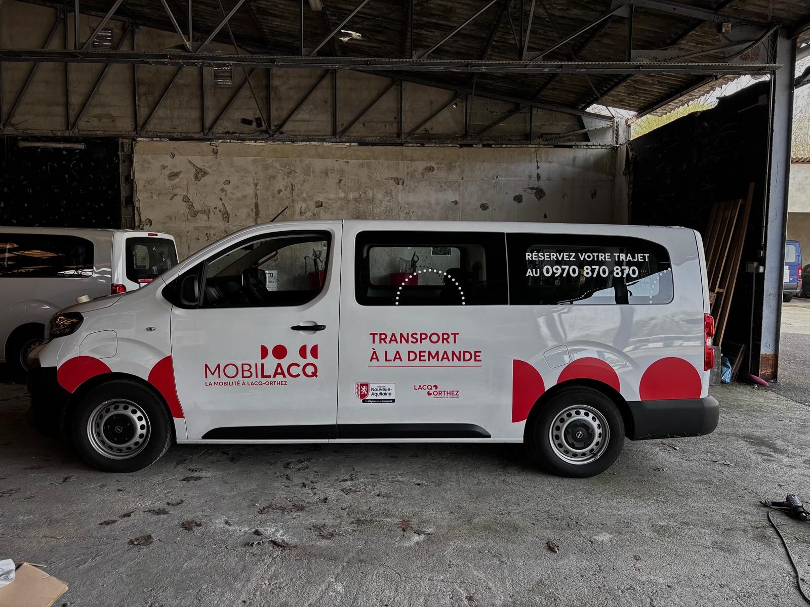 Fourgon de transport blanc et rouge stationné dans un garage, portant les inscriptions MOBILIDAD et TRANSPORT A LA DEMANDE.