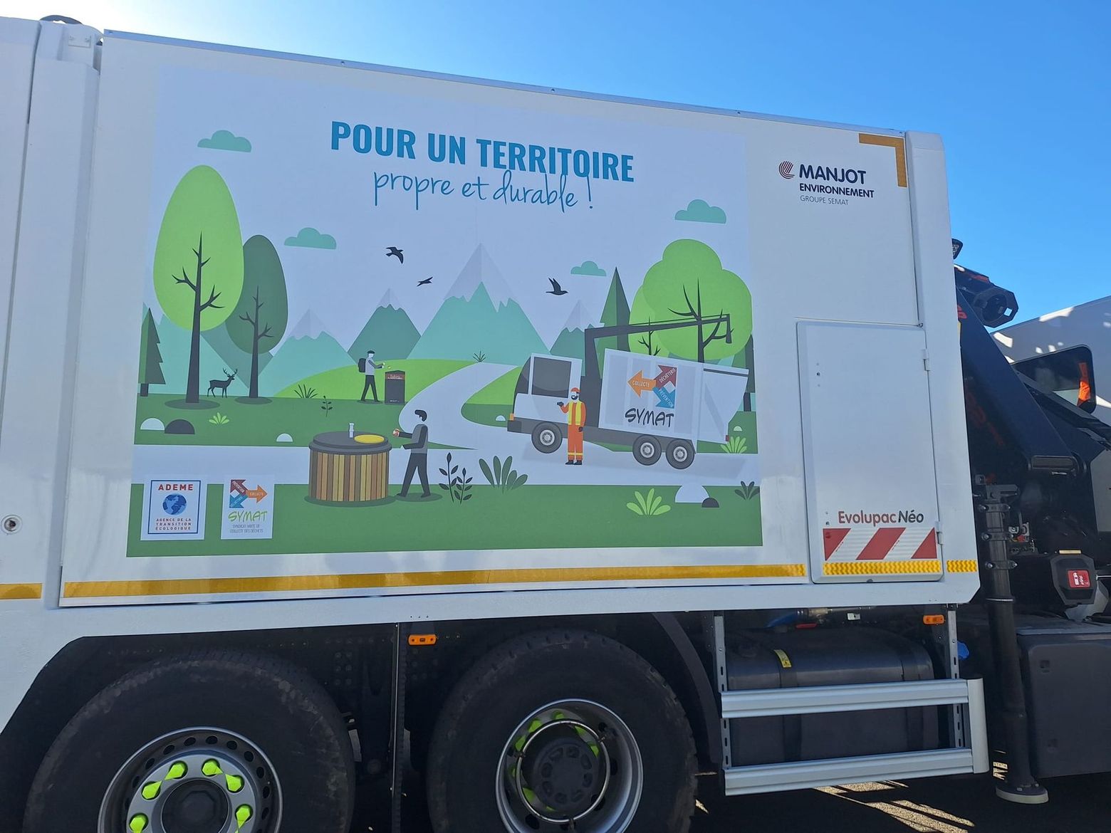 Camion-poubelle orné d'une fresque murale sur le recyclage Pour un territoire, stationné à l'extérieur sous un ciel bleu