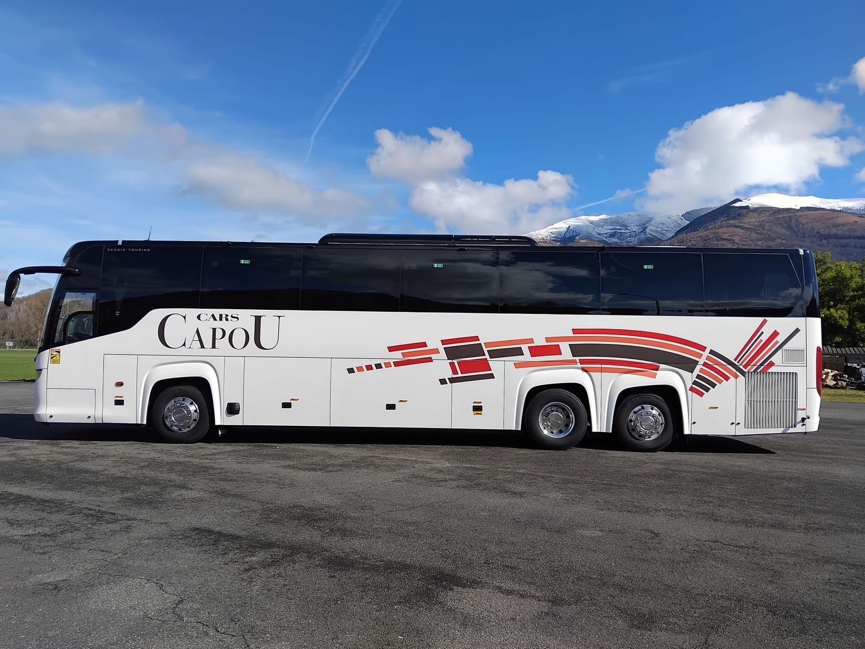 Autocar blanc de la compagnie CAPU stationné sur un terrain gravillonné sous un ciel bleu nuageux