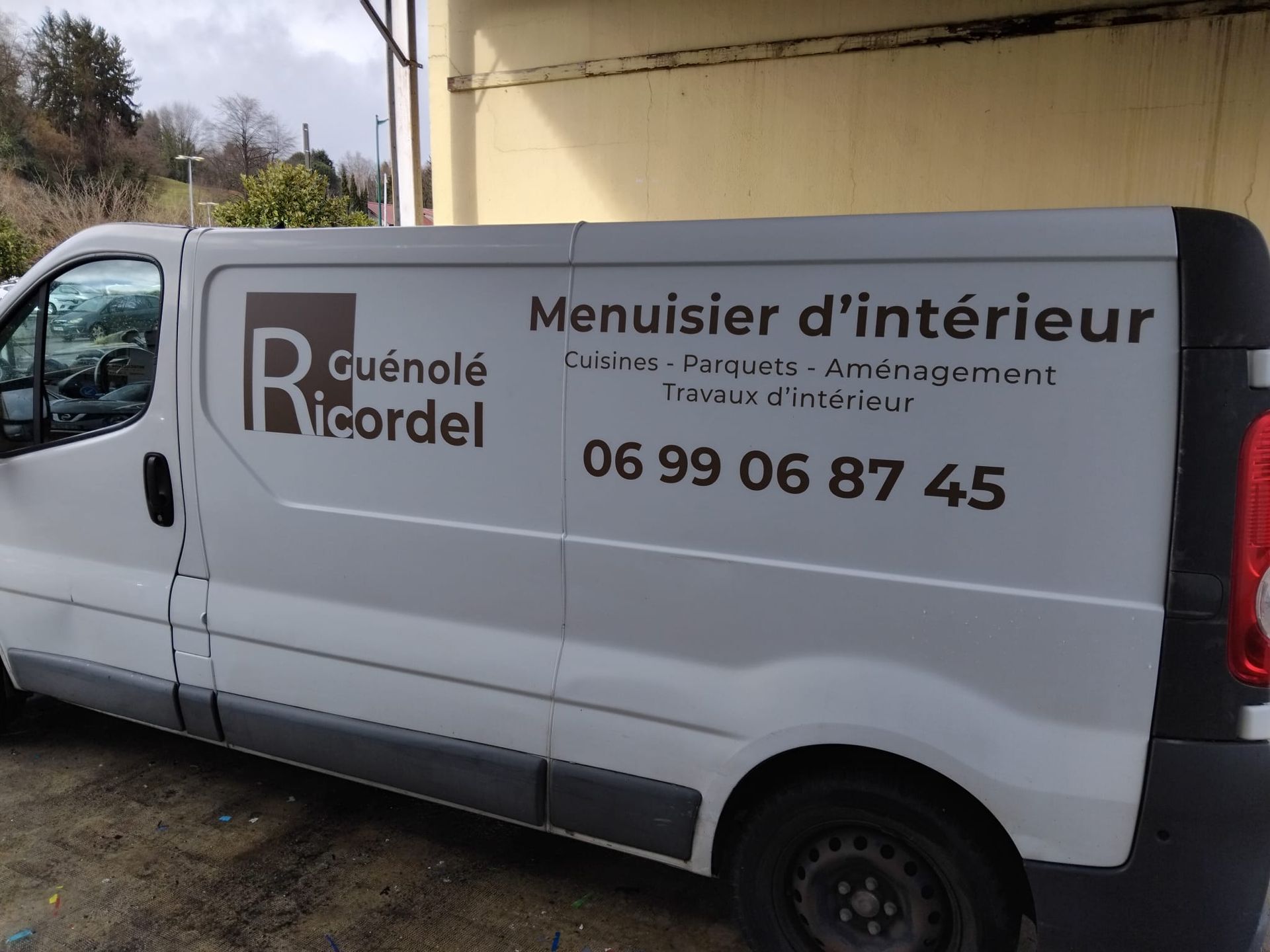 Camionnette de service blanche avec inscription Menuisier d'intérieur et numéro de téléphone stationnée à l'extérieur.