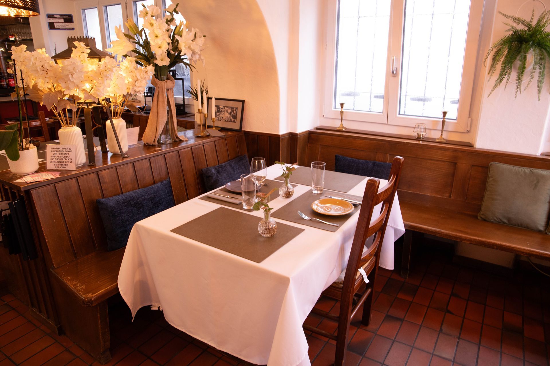 Restaurantfassade mit grünen Fensterläden, ein weisses Gebäude, Sitzgelegenheiten im Freien und Bäume.