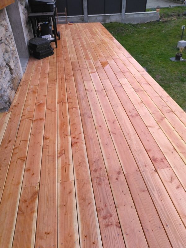 Terrasse en bois fraîchement teintée à côté d'une maison et d'une cour gazonnée
