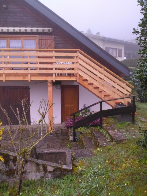 Escalier en bois et balcon donnant sur une cour gazonnée