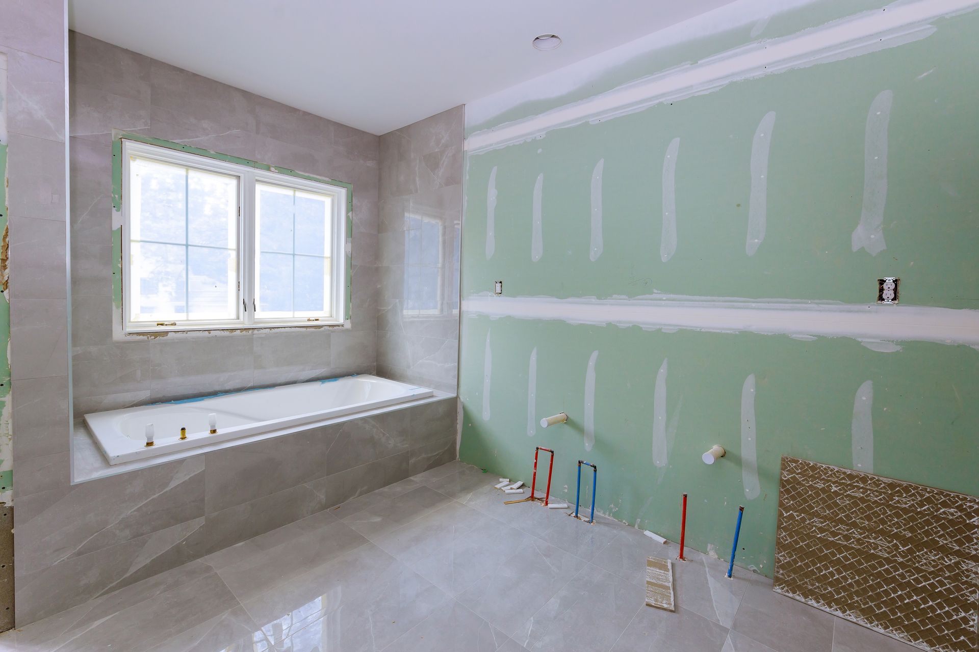 Salle de bains en rénovation avec cloisons sèches, baignoire carrelée et éclairage par fenêtre.