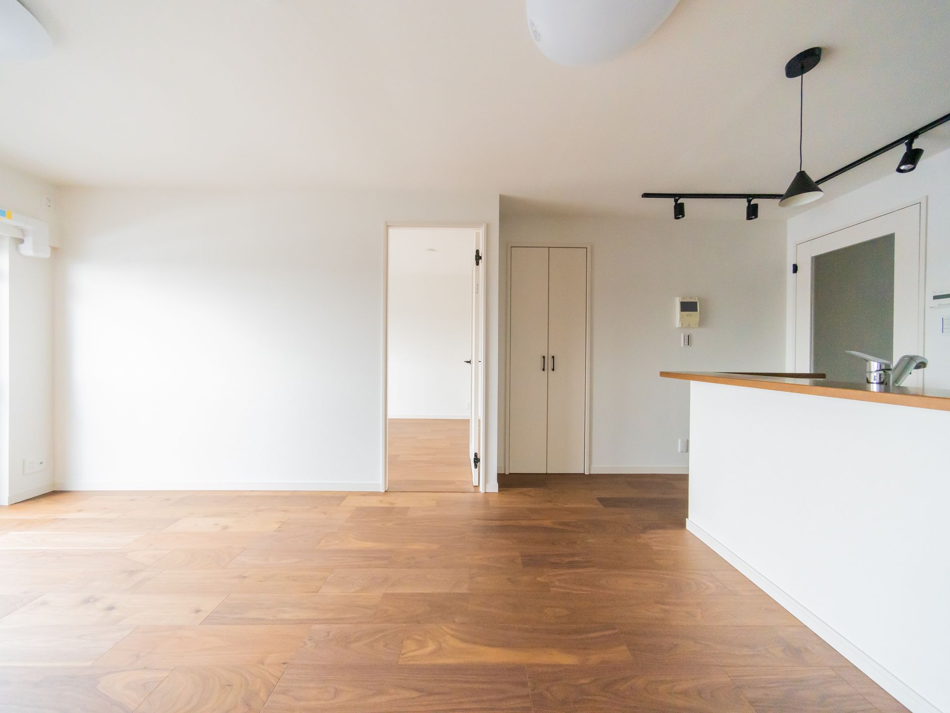 Salon moderne vide avec parquet, murs et comptoir de cuisine avec éclairage sur rail.