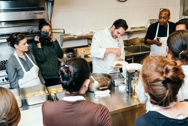 Un grupo de personas está observando a un chef preparando comida en una cocina.