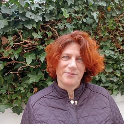 Una mujer con cabello rojo está parada frente a un arbusto.