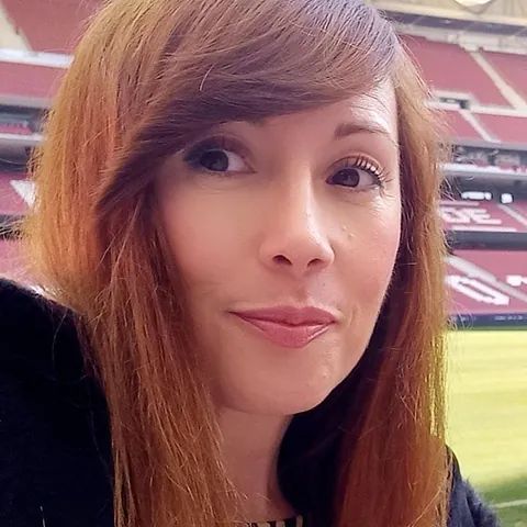 Un primer plano del rostro de una mujer con un estadio al fondo.