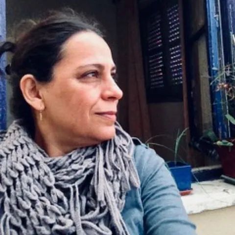 Una mujer que lleva una bufanda está sentada frente a una ventana.