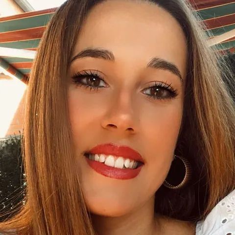 Un primer plano del rostro de una mujer con lápiz labial rojo y pendientes de aro.