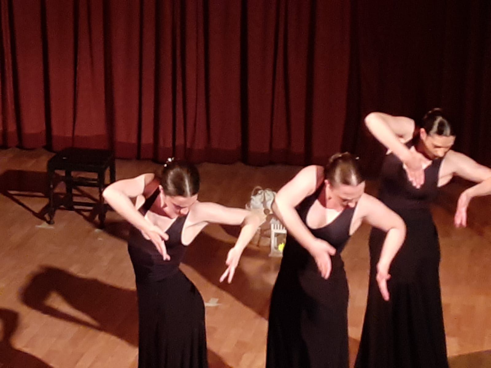 Tres mujeres con vestidos negros bailan en un escenario.