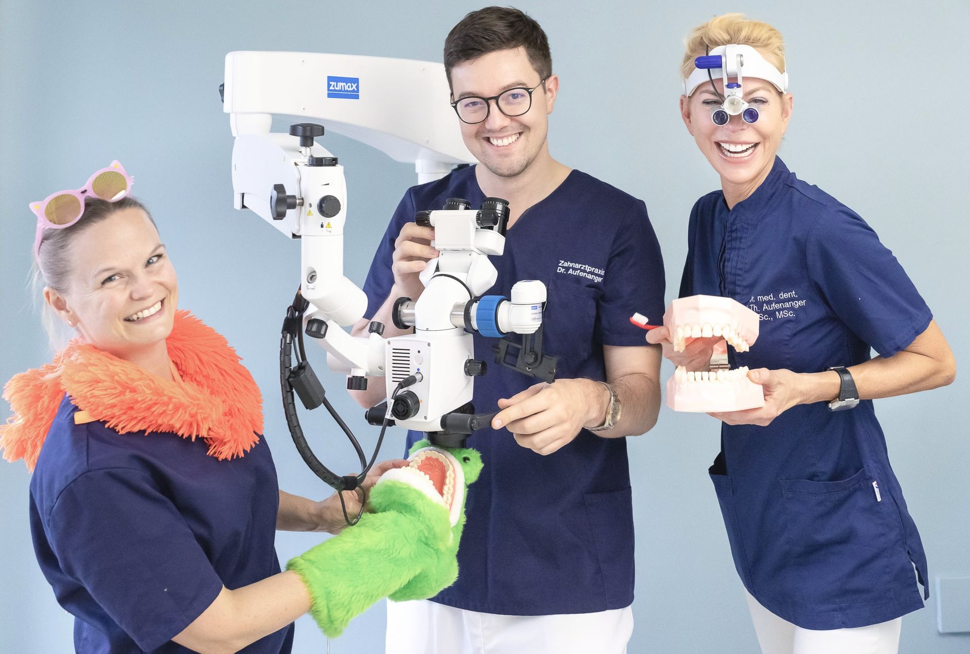 Eine Gruppe von Zahnärzten steht nebeneinander und hält Zahnmodelle und ein Mikroskop in den Händen.