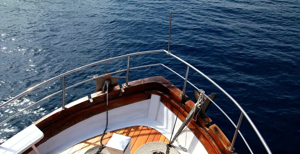 Catamarán navegando en aguas turquesas cerca de una playa con acantilado rocoso.