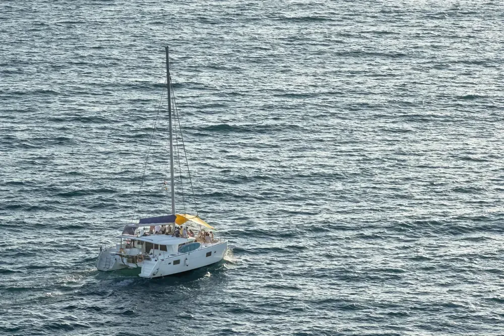 Barcos en tranquilas aguas turquesas, edificios blancos y colinas verdes en un pueblo costero.