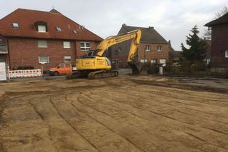 Bagger auf einem sandigen Bereich vor einem Haus